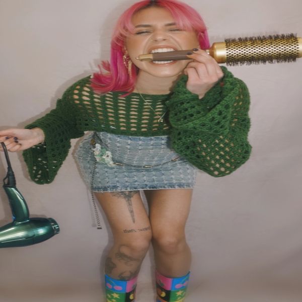 Person with pink hair holding a hairdryer and a round brush.