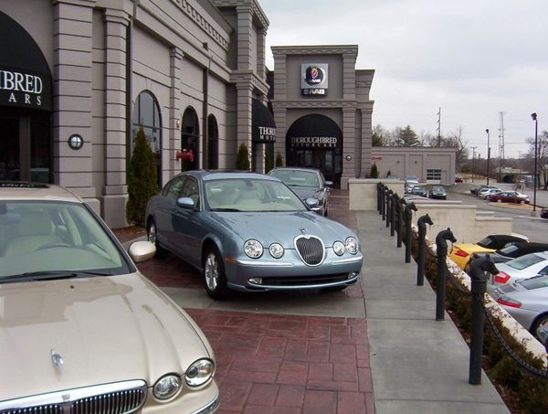 Luxury cars parked outside a Thoroughbred Motors dealership on a cloudy day.
