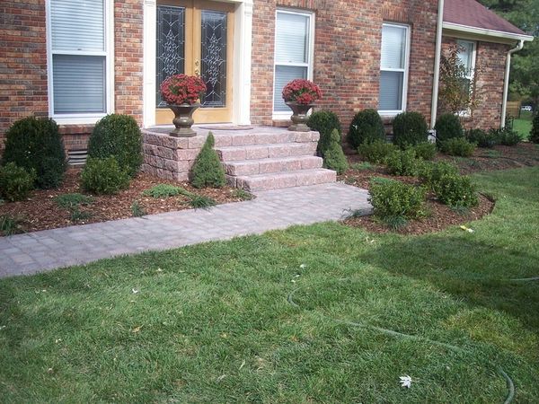 Neatly landscaped front yard with brick walkway and steps leading to a door.