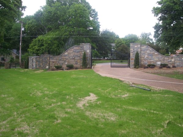 Stone entrance gate with curved walls and a driveway.