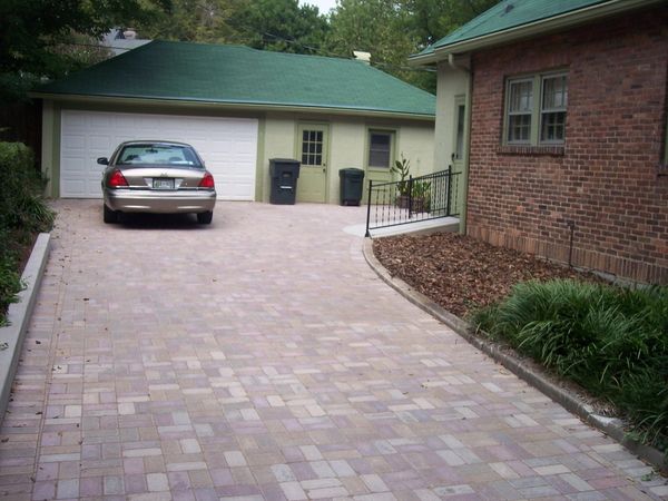 Car parked in front of a garage with a paved driveway and brick house.