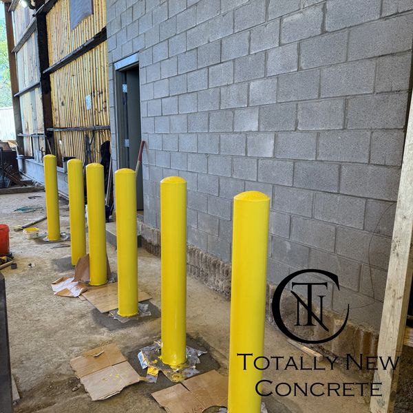New yellow bollards installed along a concrete wall in an industrial setting.