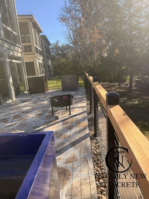 Sunlit patio with stamped concrete, modern railing, and outdoor fire pit under trees.