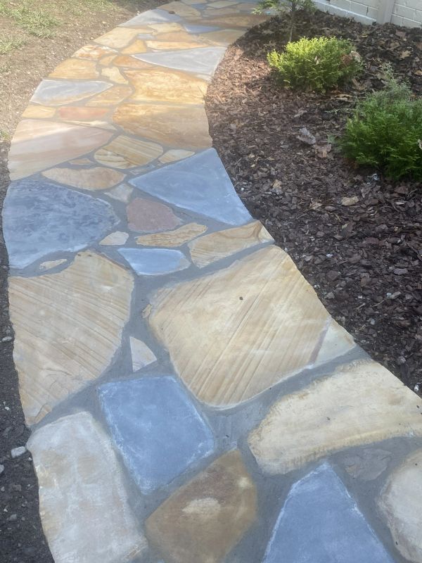 A winding stone pathway with mixed colors beside a mulched garden bed.