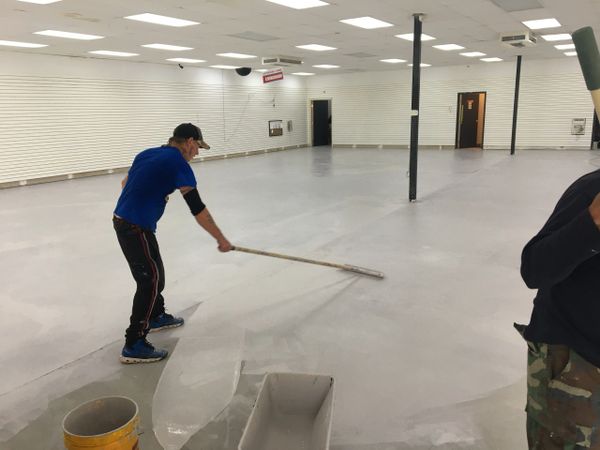 A man smooths the floor in an empty store with a long tool.