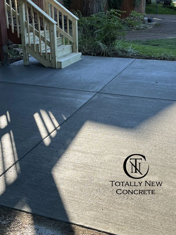 Newly poured concrete patio with wooden stairs and shadow patterns.