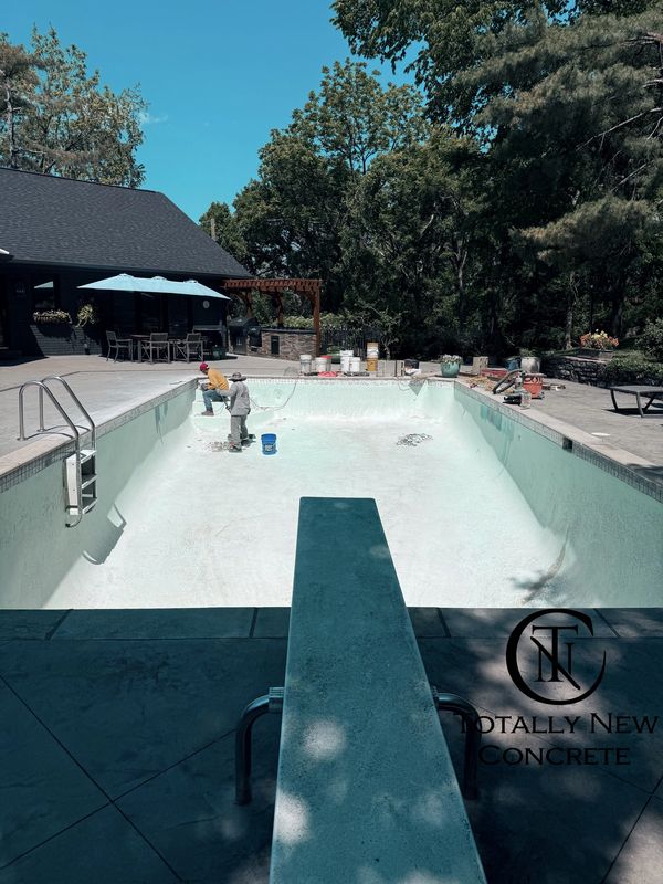 Workers refurbishing an empty residential swimming pool on a sunny day.