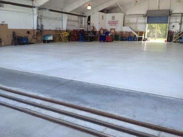 Large empty warehouse space with concrete floor and some equipment along the walls.