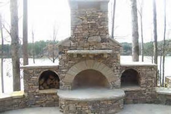 Outdoor stone fireplace with wood storage on each side near a lake.