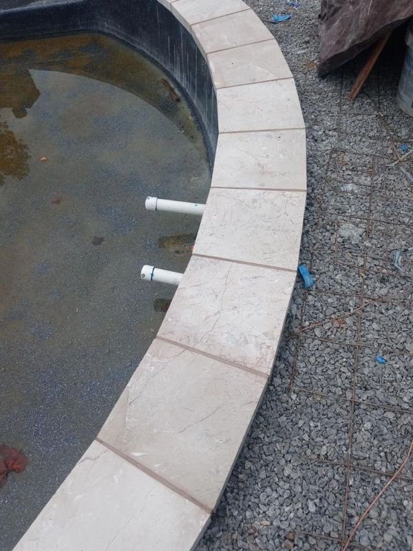 Curved tile edge of an unfinished pool with gravel and pipes.