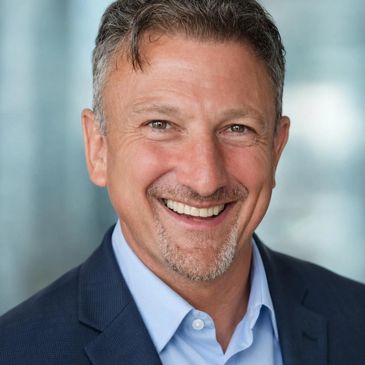 Smiling man in a suit with a blurred background.