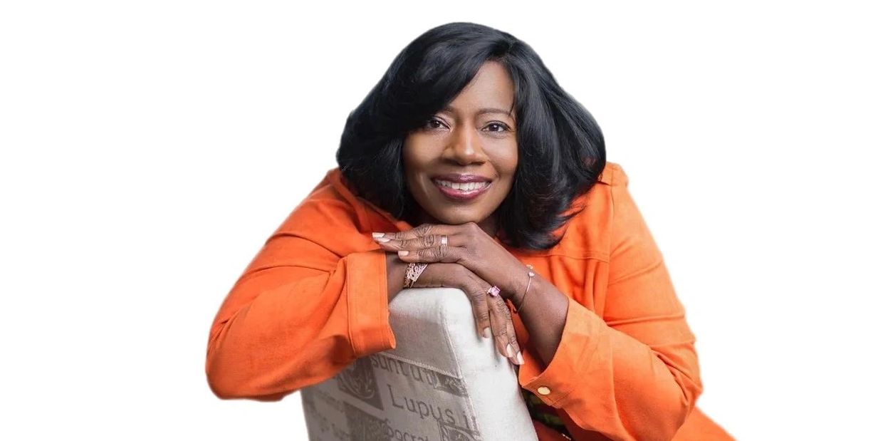 Woman in orange leaning on a chair with a smile.