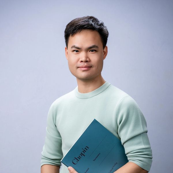 Young man holding a book titled 'Chopin' against a plain background.