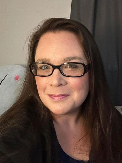 A woman with glasses and long brown hair smiling at the camera.