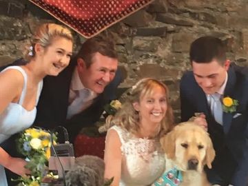 A joyful wedding scene with a bride, groom, guests, and two dogs.