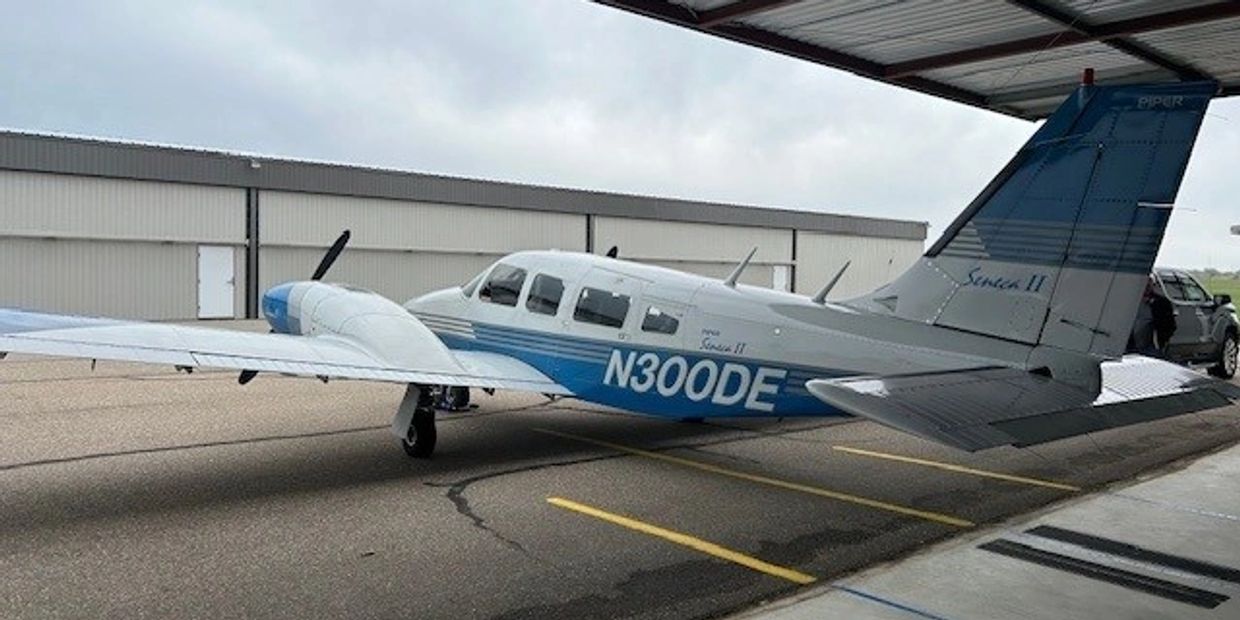 Small twin-engine Piper aircraft parked near hangar.