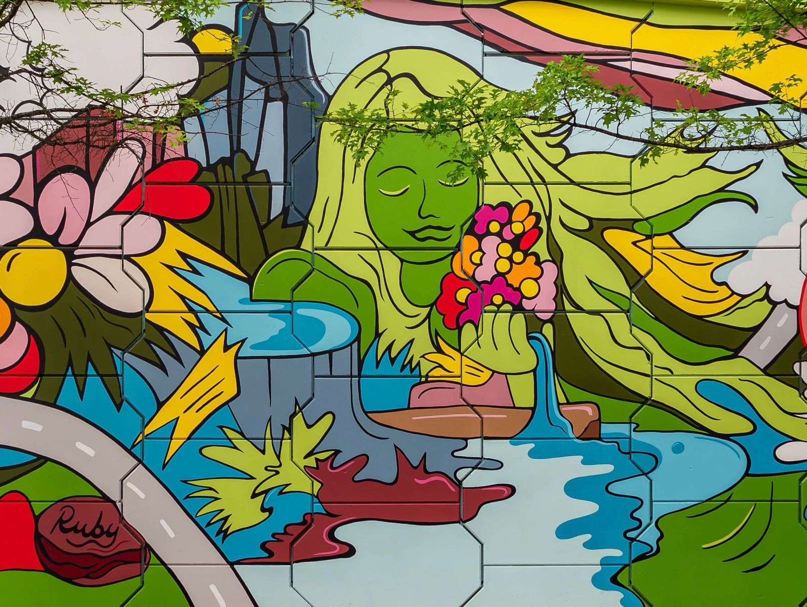 Colorful mural of a green woman holding flowers by a river.