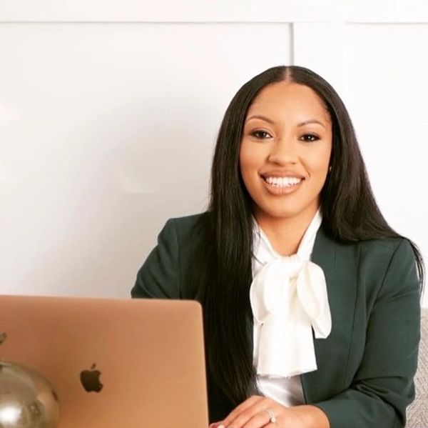 Confident woman in business attire smiling at her desk with a laptop.