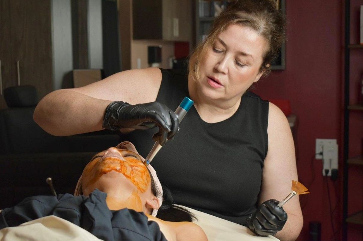 A woman wearing a black top is using a tool during a facial