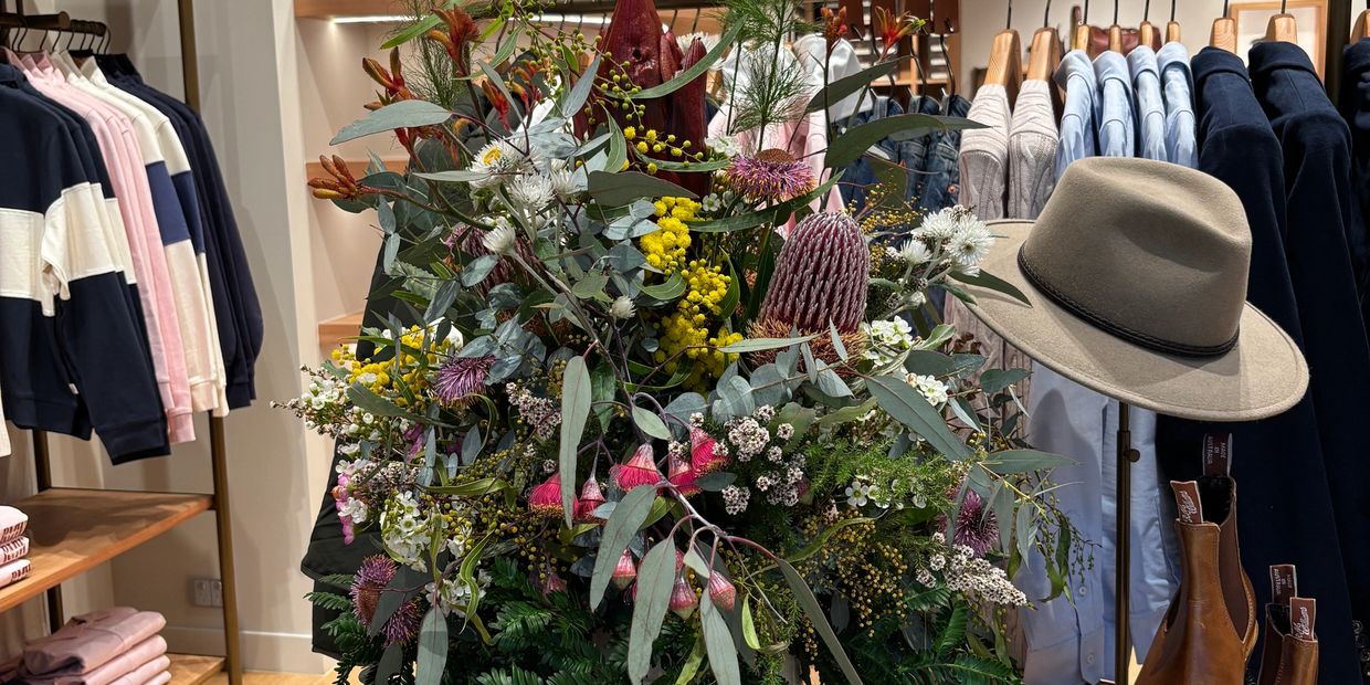 A floral arrangement with various clothing items and a hat in the background.