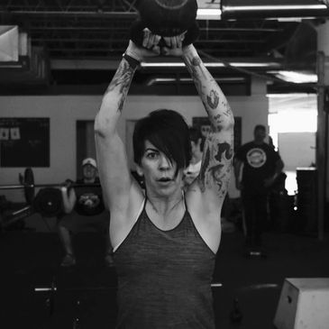 Woman doing using a kettlebell, a man uses a barbell in the background