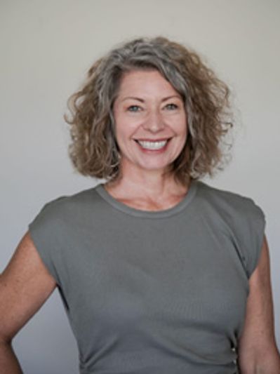 Smiling woman with curly hair in a gray top against a neutral background.