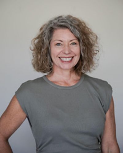 Smiling woman with curly hair in a gray top against a neutral background.