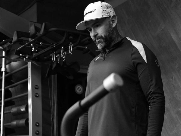 Man in a cap looking at gym equipment thoughtfully.
