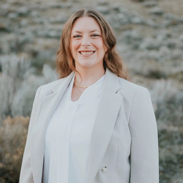 Smiling woman in a light gray blazer outdoors.