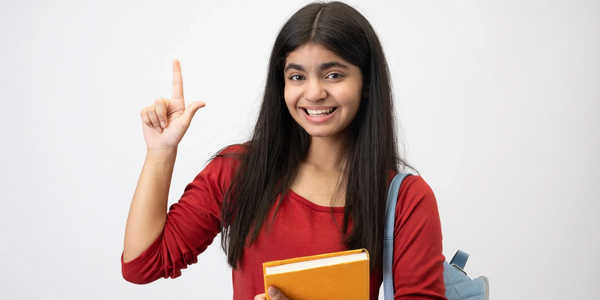 Smiling student holding a book and pointing up with her finger.
