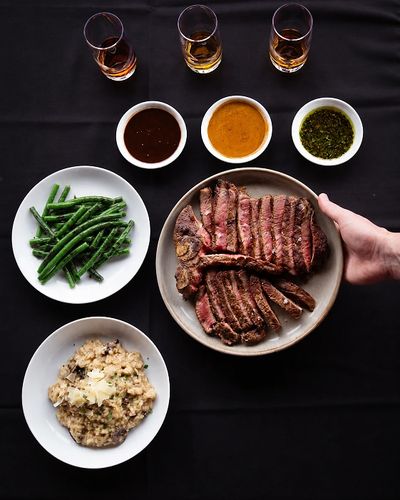 A steak dinner with sides and sauces arranged on a black tablecloth.