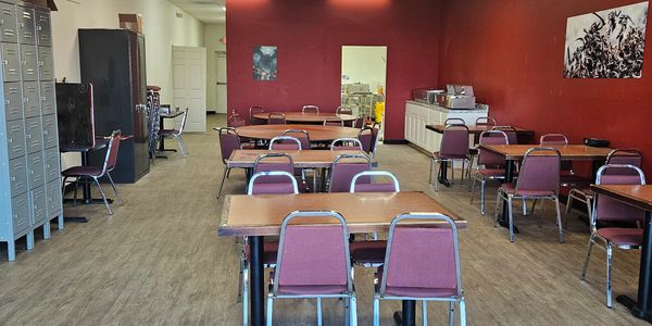 Empty cafeteria with red walls and multiple tables and chairs.