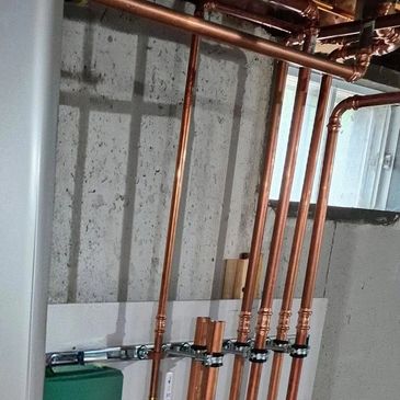 Neatly arranged copper pipes installed along a concrete wall in a utility room.