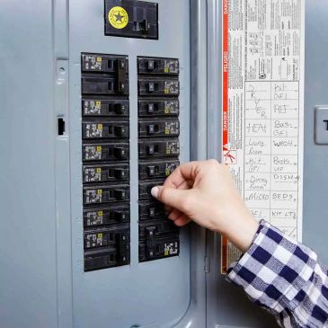 Person adjusting a circuit breaker in an electrical panel.