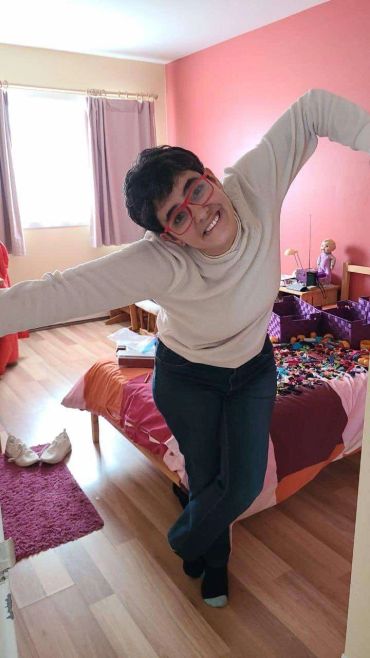Person with red glasses posing joyfully in a colorful bedroom.