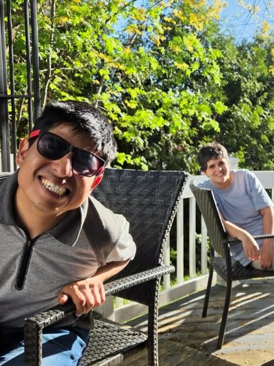Two boys smiling and sitting on outdoor chairs on a sunny day.