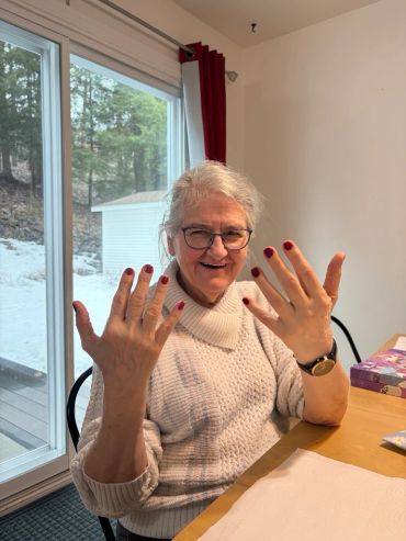 Elderly woman joyfully showing her freshly painted red nails.