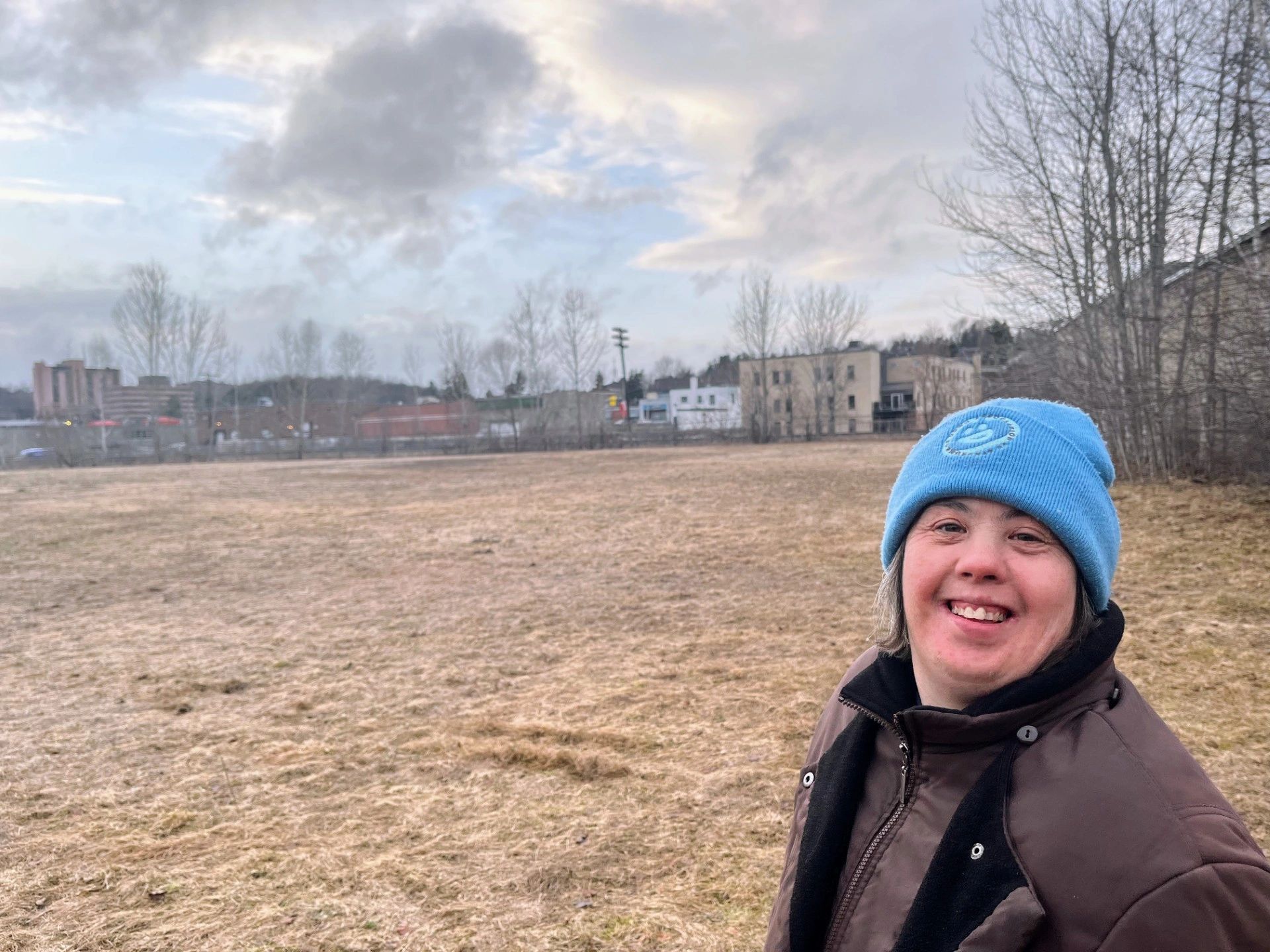 Smiling person in a blue beanie outdoors on a cloudy day.