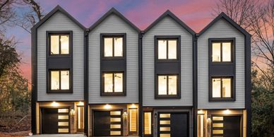 Modern four-unit townhouse complex at sunset with illuminated windows.
