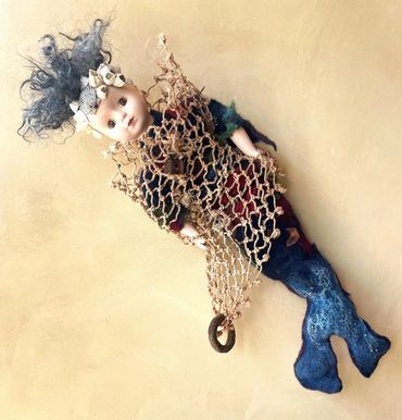 A discarded porcelain doll morphed into a mermaid encumbered by ocean detritus.
