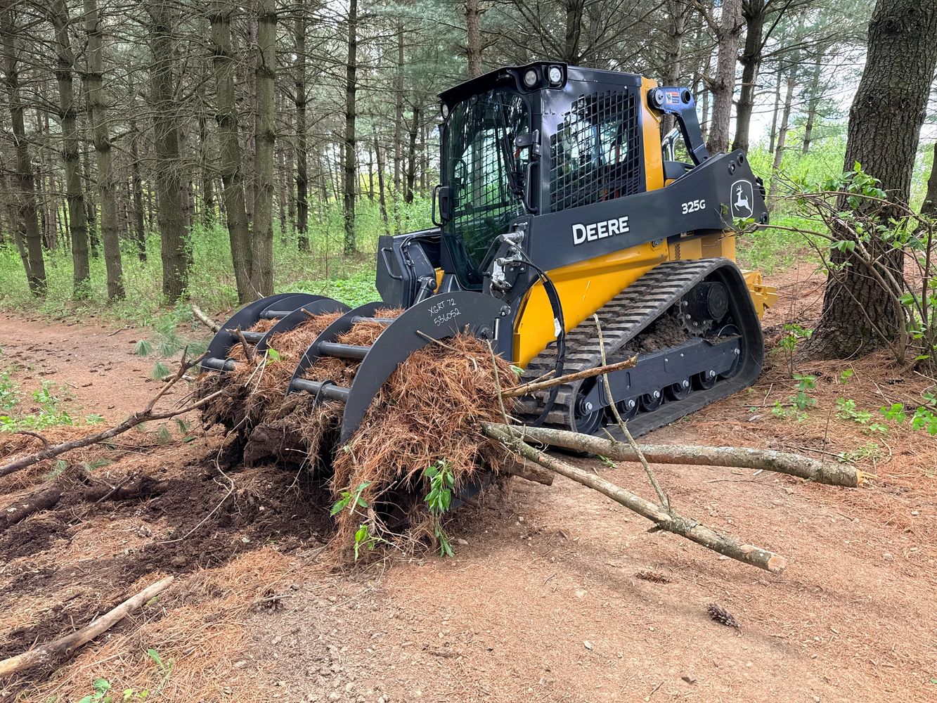 John Deere 325G skid steer loader clearing forest debris.