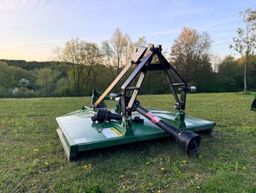Green rotary mower attachment on grass under a clear sky.