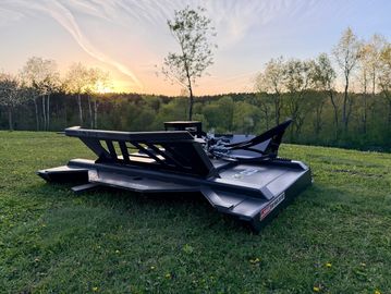 Sunset behind a black lawn mower on green grass.