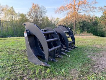 Close-up of heavy-duty grapple attachments on grass with trees in background.