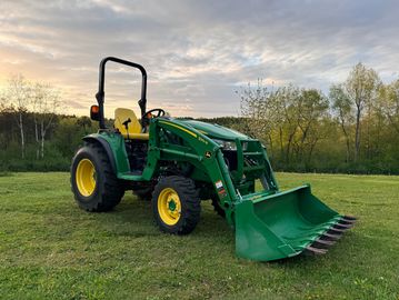 Green tractor with front loader on grassy field at sunset.