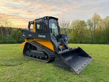 A Deere 325G compact track loader on grass at sunset.