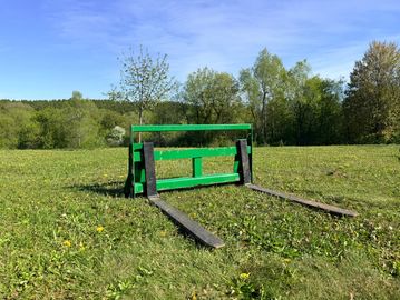 A green wooden pallet fork attachment on grass under a clear sky.