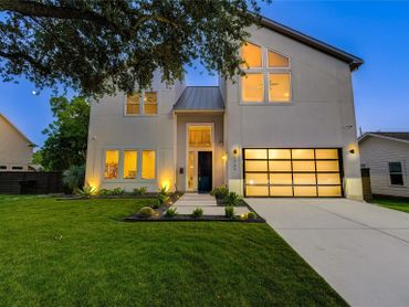 Modern two-story house with illuminated windows and a well-kept lawn at dusk.