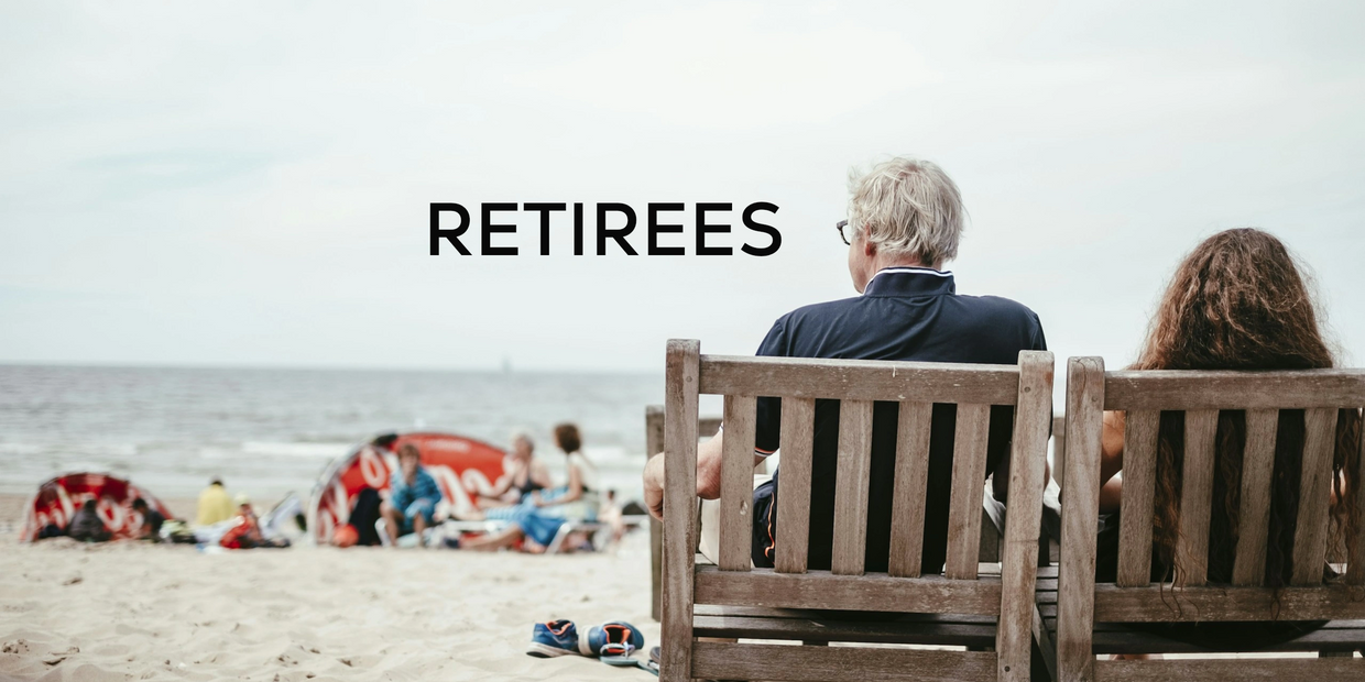 A man and woman sitting in wooden chairs on a beach with the word 'RETIREES'