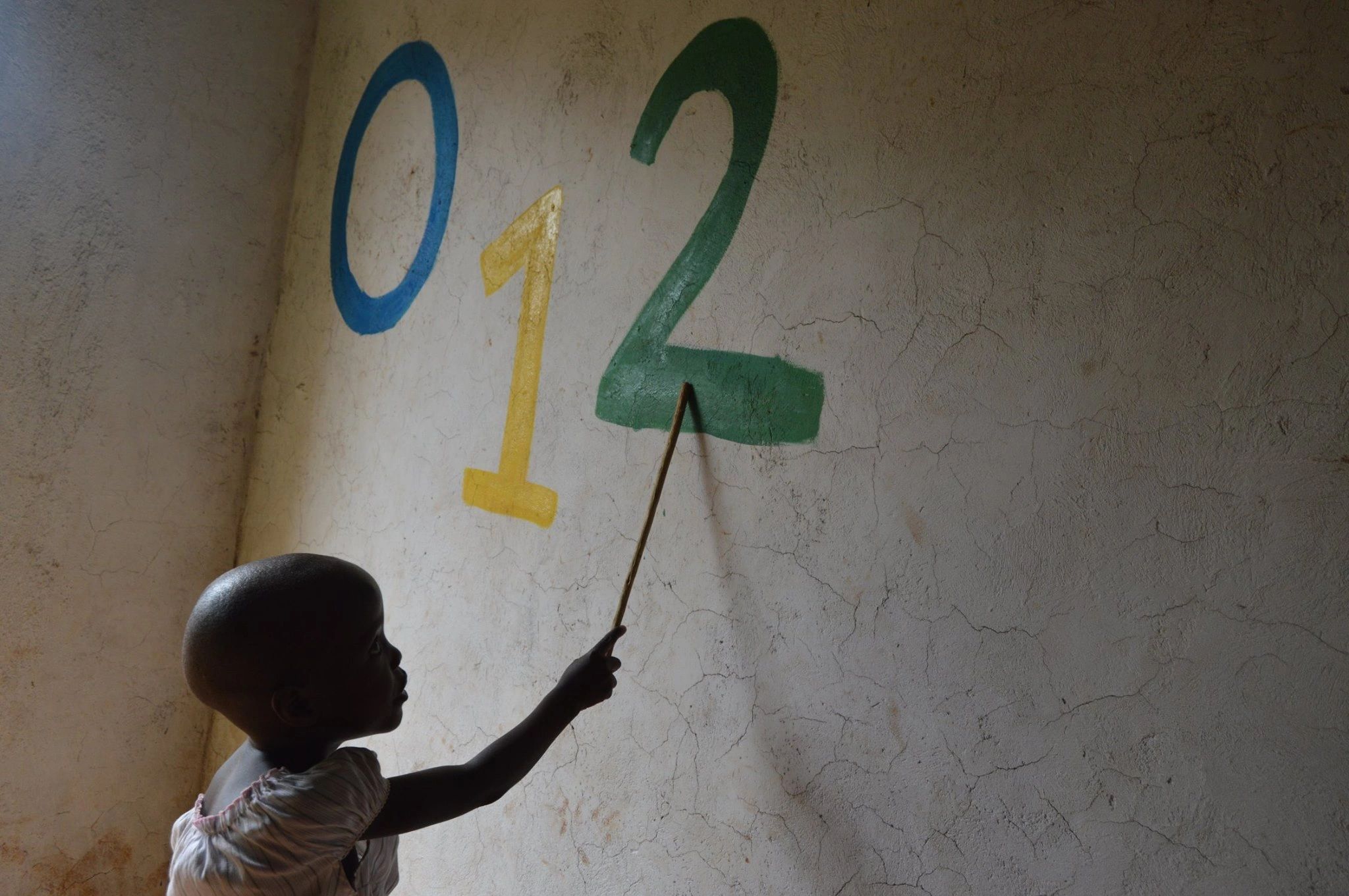 Child pointing at colorful numbers 0, 1, 2 on a wall.